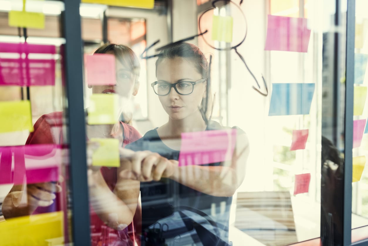 Two office workers pasting sticky notes to a window
