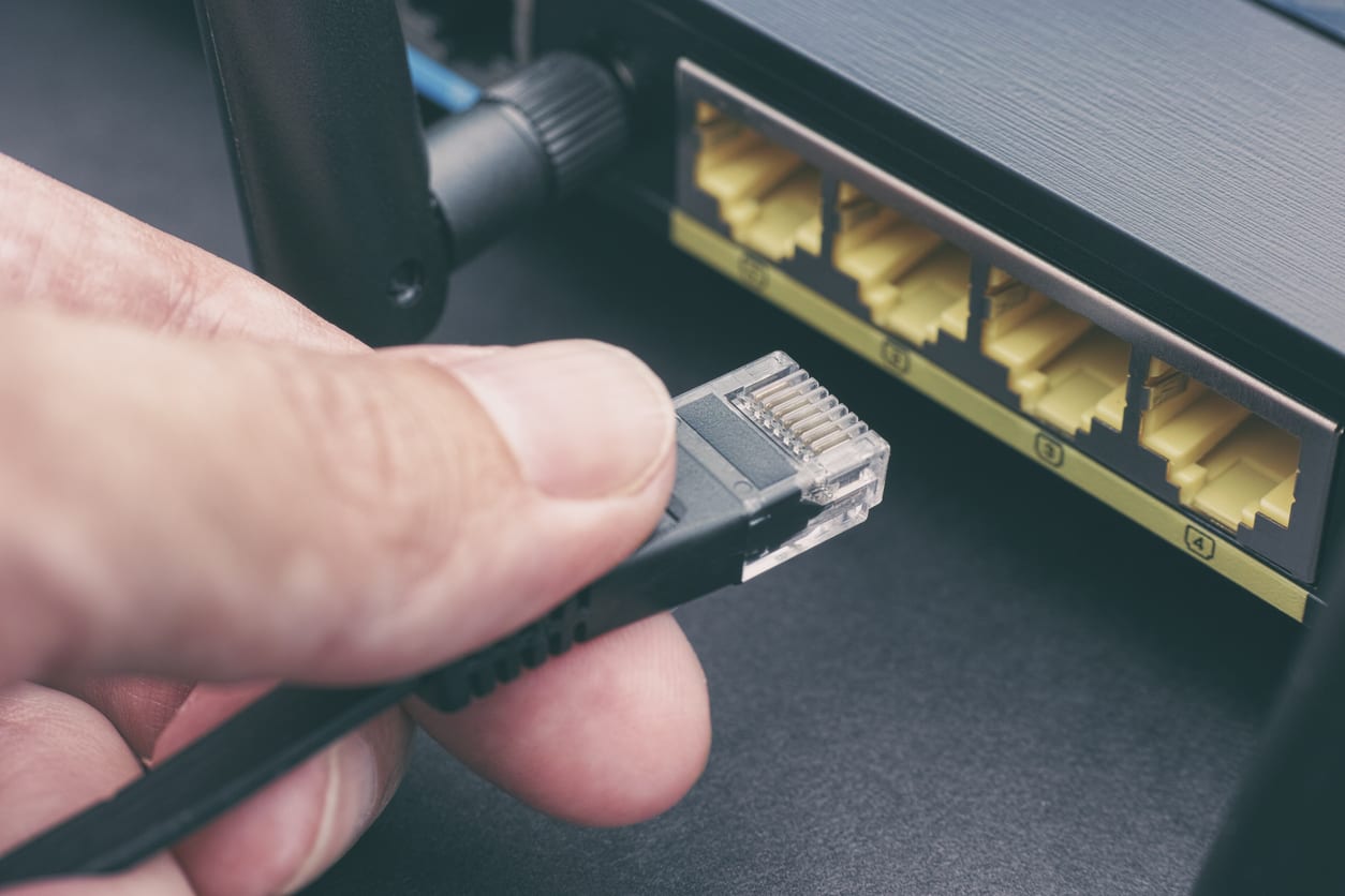 a man's hand about to plug a cable into a router's ethernet port