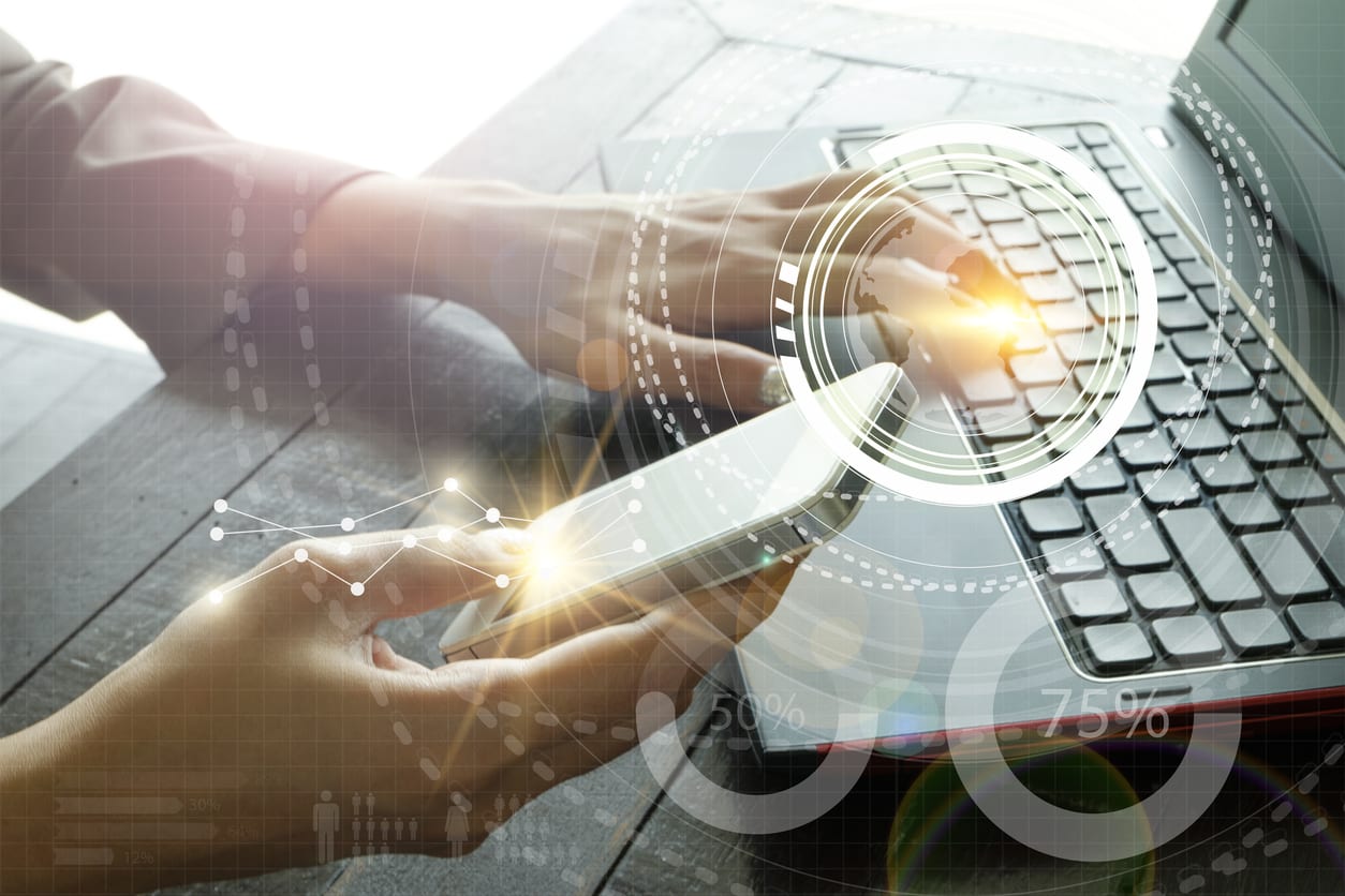 woman's hands, one on laptop keyboard and the other holding a smart phone