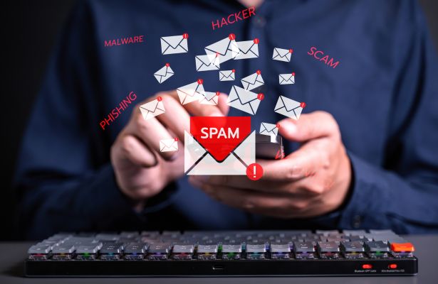man typing on mobile phone next to a keyboard and mail images are scattered around the phone with each mail icon displaying text of a email cyber threat.