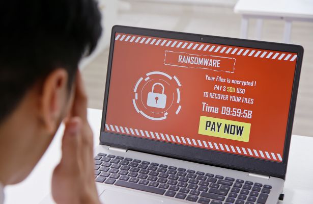 man looking stressed while looking at a laptop screen which displays the words 'ransomware'. indicating he needs to pay the fees to get his files back
