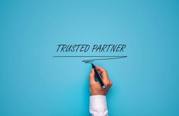 hand using a black pen to write trusted partner on a blue background