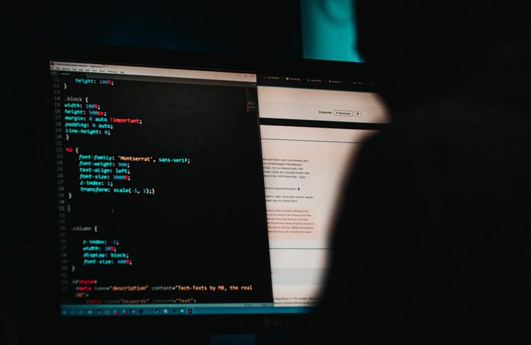 man sitting in dark room, working on computer code